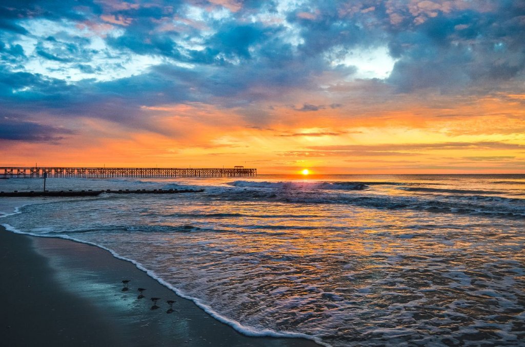 A pawleys island sunrise casts vibrant colors over the ocean, with a serene pier silhouetted against the glowing sky.